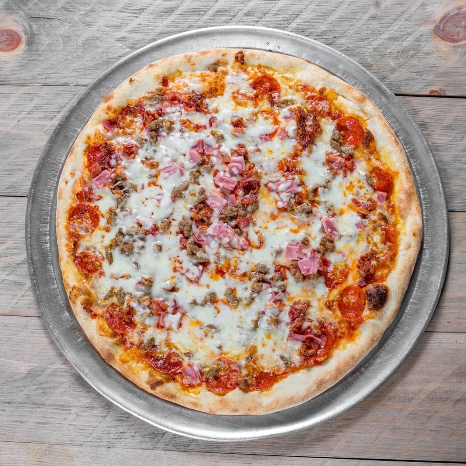 A whole meat lover's pizza with pepperoni, ham, and sausage on a metal pan.