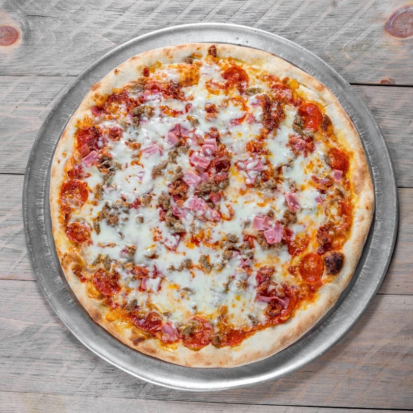 A whole meat lover's pizza with pepperoni, ham, and sausage on a metal pan.