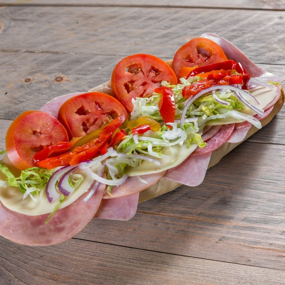 A large, colorful sub sandwich filled with meats, cheeses, tomatoes, lettuce, onions, and peppers.