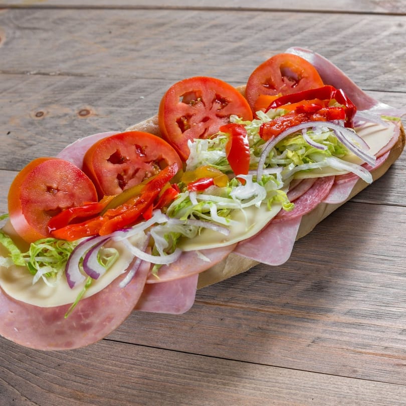 A large, colorful sub sandwich filled with meats, cheeses, tomatoes, lettuce, onions, and peppers.